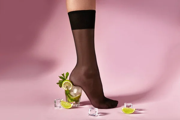 Nylons, stay-up, tights, hosiery, hose, pantyhose socks summer collection on pink background as a heel creative a glass of cocktail mojito with lime lemon mint and ice.