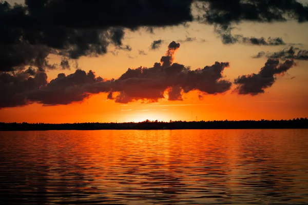 Orange Sky Glows Over Water as Sun Drops Behind the Horizon behind Rainy Lake