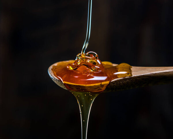 Strand of Honey Piles Into Wooden Spoon against dark background