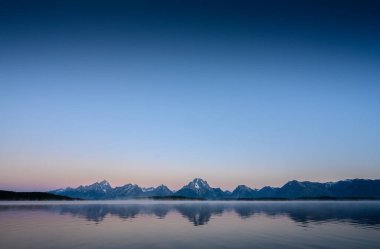 Tetons ve Jackson Gölü 'nde Sabah Güneşinin Doğuşu. Gölde hafif bir sis dalgası var.