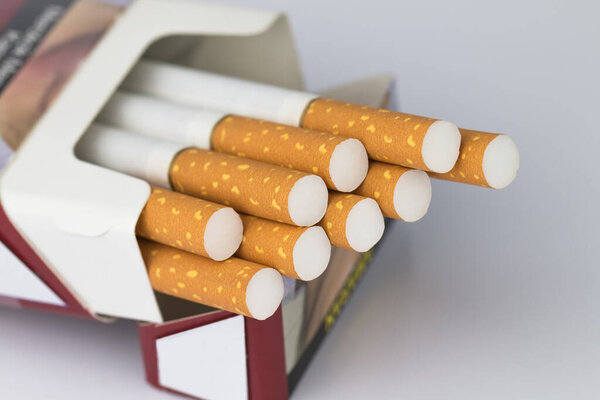 Cigarettes packed in red paper envelopes The cigarette end or cigarette end is brown and the tip is white and the end of the cigarette or cigarette end extends beyond the package on the white surface.