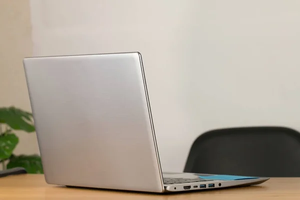 Grey notebook computer Leave it ready for work. Resting on a brown wooden office desk And there is a black chair White wall background The picture on the right is decorated with green trees.