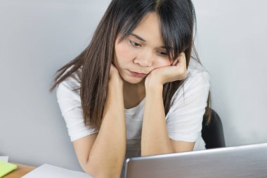 Asyalı kadınlar beyaz gömlek giyer. Evde çalışırken stresli hissediyorum ve masadaki gri dizüstü bilgisayara bakan gözler ve çeneyi tutan eller. Ve beyaz duvar arkaplanı