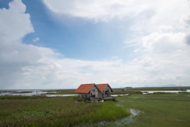 Açık gökyüzü ve güzel bulutlarla dolu bir günde gölün ortasında terk edilmiş bir ev..