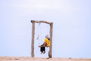 Müslüman kadınlar salıncakta oturuyor kumsalda, güzel, berrak bir gökyüzünde.