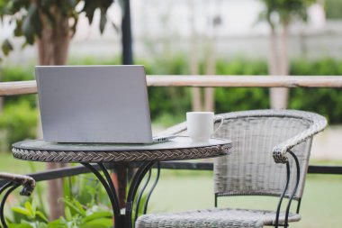 Laptop bilgisayarlar ve beyaz kahve fincanları masanın üzerinde duruyor, evin önündeki çimlerin üzerinde oturuyor, dinleniyor. Resimde hiç insan yok..