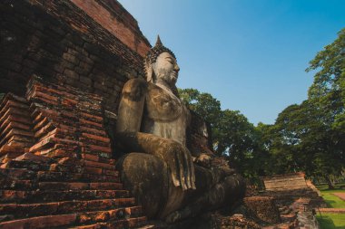Tapınaktaki büyük Buda heykeli Sukhothai Tarihi Parkı 'nda görkemli bir şekilde duruyor. Akşamları, turuncu renkli gökyüzünün ortasında Tayland 'ın Sukhothai Eyaleti.