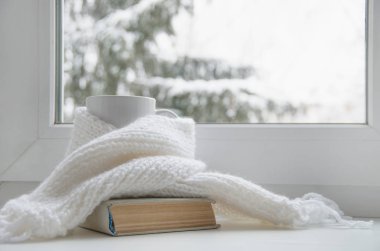 Bir kupa sıcak çay ve dışarıdaki kar manzarasına karşı cam kenarında yün örgü..