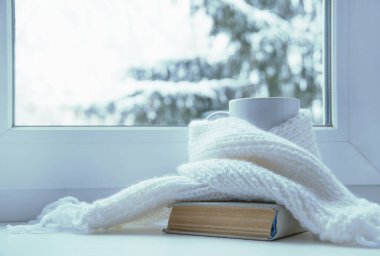 Bir kupa sıcak çay ve dışarıdaki kar manzarasına karşı cam kenarında yün örgü..