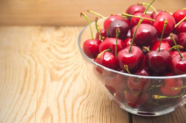Kirazlar ahşap masada, su damlaları makro arka planda.
