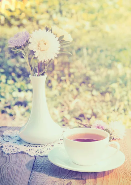 Flowers and white cup of tea on wooden table