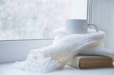 Bir kupa sıcak çay ve dışarıdaki kar manzarasına karşı cam kenarında yün örgü..