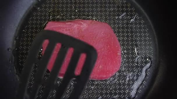 Ein Stück Thunfisch wird in Öl in einer Pfanne gebraten und mit einem Spachtel angedrückt — Stockvideo