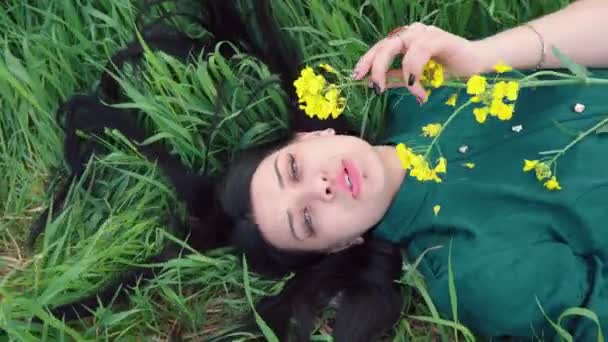 彼女の手に花を持つ美しい女性が草の中にあり 歌を歌います 長い散髪で緑のドレスの女の子 ズームアウトカメラ — ストック動画