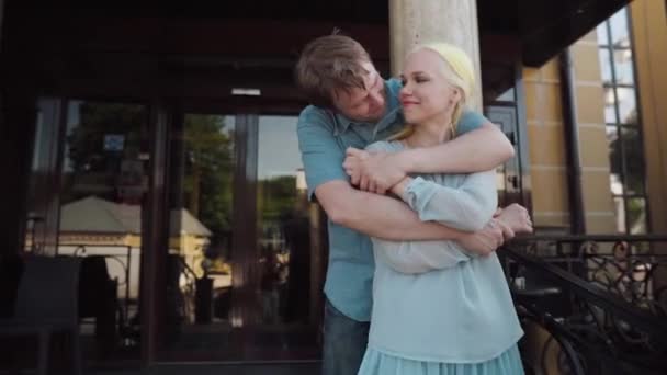 En kille och en tjej kysser vid ingången till hotellet. — Stockvideo