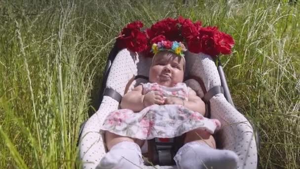 Una niña pequeña en un asiento de coche yace en la hierba . — Vídeos de Stock