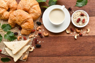 Kahvaltıda ekmek ve bir bardak soya sütü ve kruvasan ile ahşap bir masada yulaf ezmesi ve dut çileği..