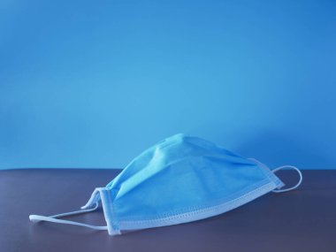 Mavi arka planda tıbbi koruyucu maske. Tek kullanımlık yüz maskesi ağız ve burnu kapatır..