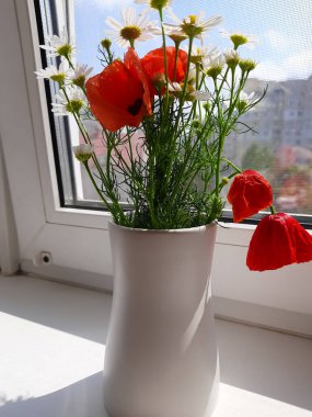 Penceresinde vazoda haşhaş olan bir buket papatya..