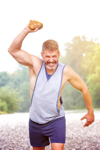 bearded handsome athlete throwing agressivley a stone outdoors