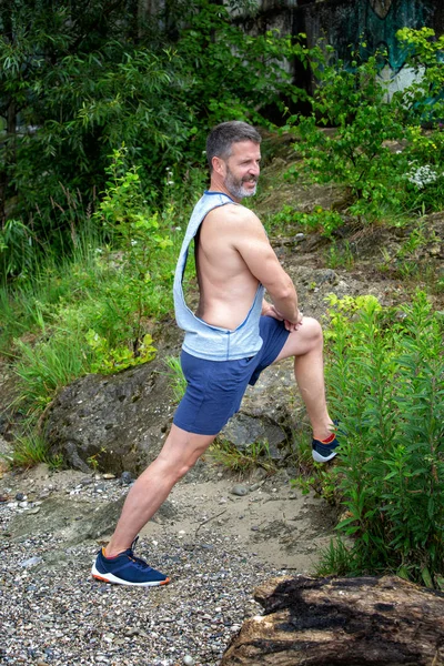 handsome bearded athlete standing outdoors and stretching