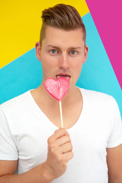 Portrait Handsome Blond Man Licking Heart Shaped Lollipop — Stock Photo, Image
