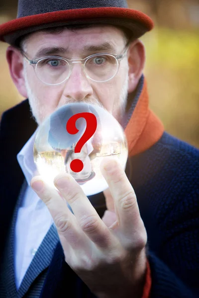 mature businessman looking at a glass sphere with red question mark