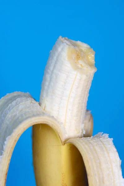 Полусъеденный очищенный банан на синем фоне — стоковое фото