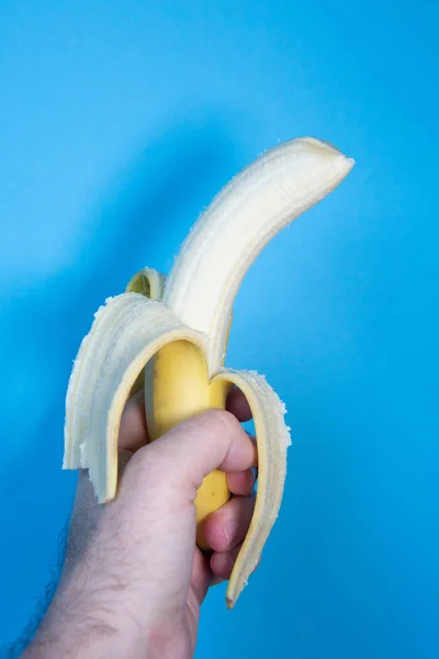 Рука держа очищенный банан на синем фоне — стоковое фото