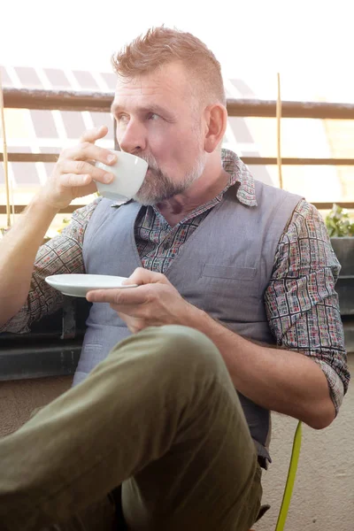 Man in his 50s sitting on balcony and drinking coffee — Stock Photo, Image