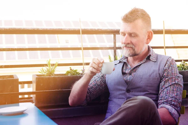 Man in his 50s sitting on balcony and drinking coffee — Stock Photo, Image