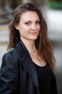 Deri ceketli genç esmer kadın dışarıda bekliyor.