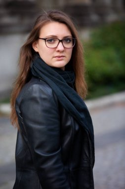 Deri ceketli genç esmer kadın dışarıda bekliyor. 