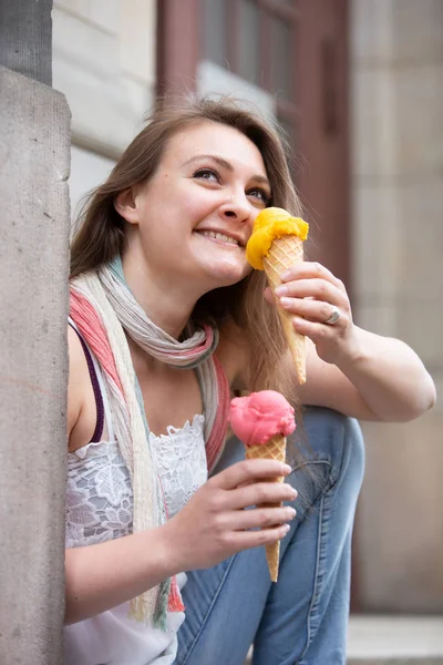 Jovem mulher sentada ao ar livre com dois cones de sorvete — Fotografia de Stock