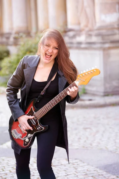 Young woman in black leather jacket playing the guitar outdoors — 스톡 사진