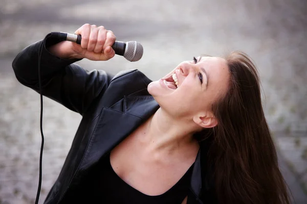 Jeune femme brune chantant avec microphone en plein air — Photo