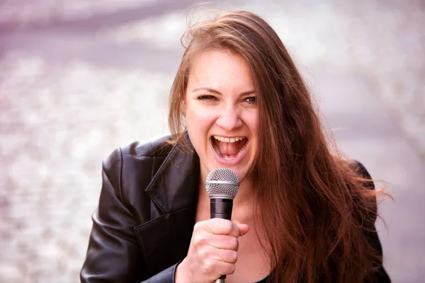 Genç esmer kadın mikrofonla dışarıda şarkı söylüyor. — Stok fotoğraf