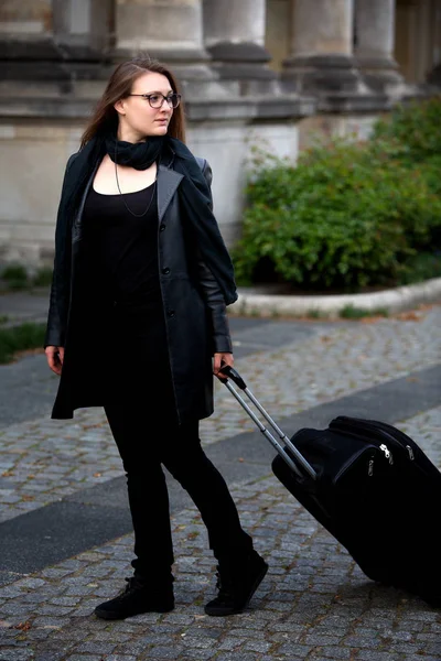 Mladá žena v černé kožené bundě chůze s kufrem — Stock fotografie