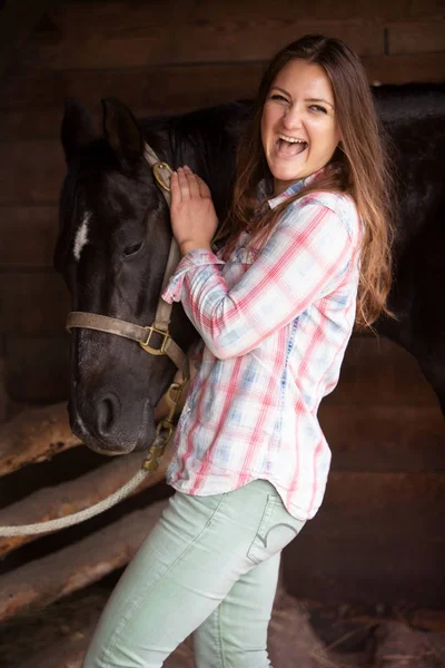 Young woman standing with her black horse and laughs — Stock Photo, Image