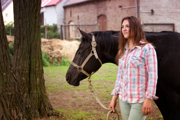 Young woman standing outdoors with her black horse — Stock Photo, Image