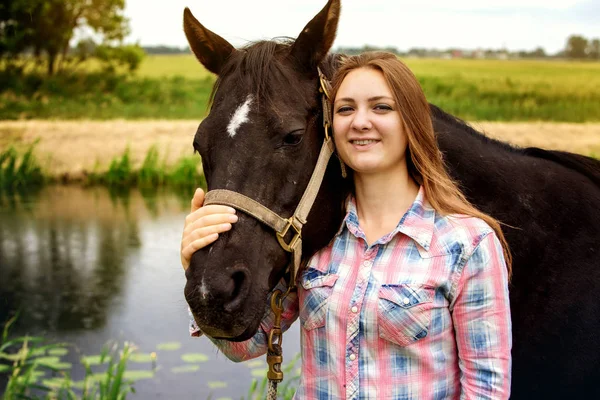 Young woman standing outdoors with her black horse — Stock Photo, Image
