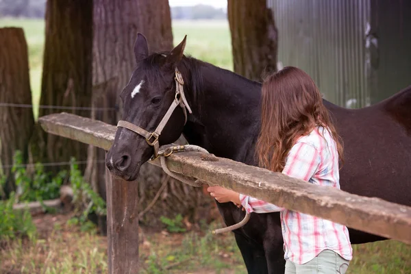Young woman standing outdoors with her black horse — Stock Photo, Image