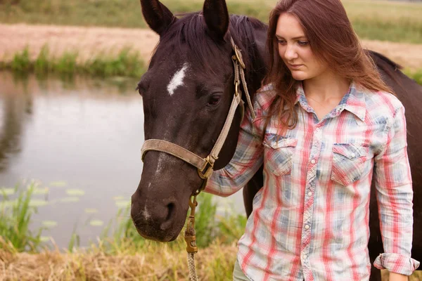 Young woman standing outdoors with her black horse — Stock Photo, Image