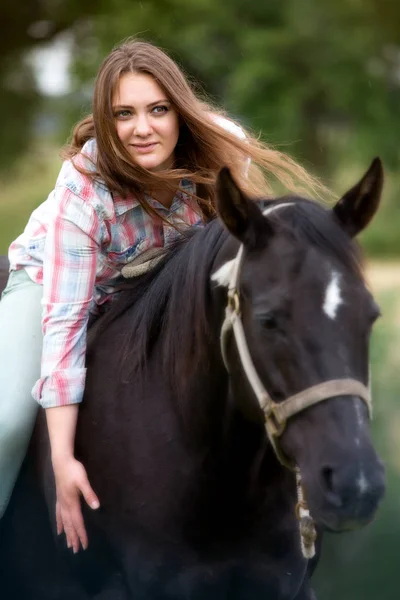 Young woman sitting on her black horse — Stock Photo, Image