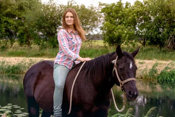 Young woman sitting on her black horse — Stock Photo, Image