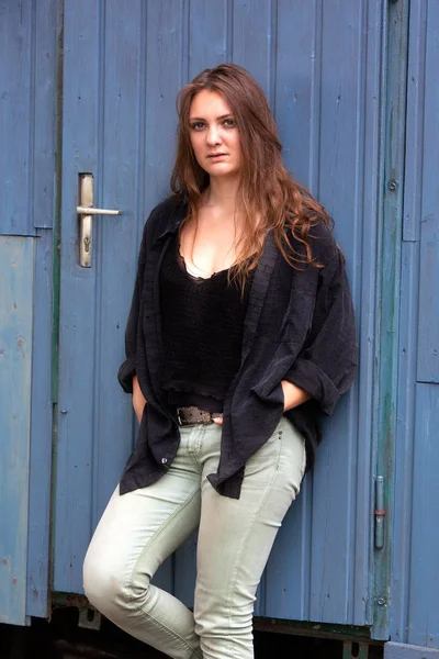 Brunetka mladá žena stojící venku u modrých dřevěných dveří — Stock fotografie