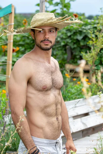 Όμορφος άνθρωπος χωρίς μπλούζα με ψάθινο καπέλο στέκεται στον κήπο — Φωτογραφία Αρχείου