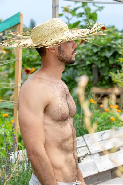庭に立つわら帽子を持つハンサムなシャツレスの男 — ストック写真