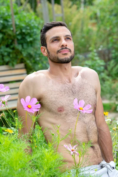 Bell'uomo senza camicia con la barba seduto fuori in giardino — Foto Stock