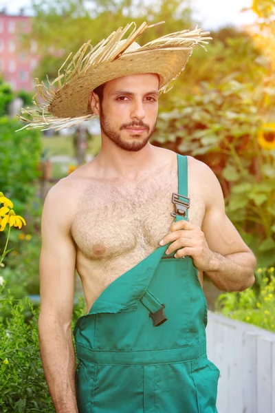 Handsome gardener with green pants and straw hat standing in gar — Stock Photo, Image